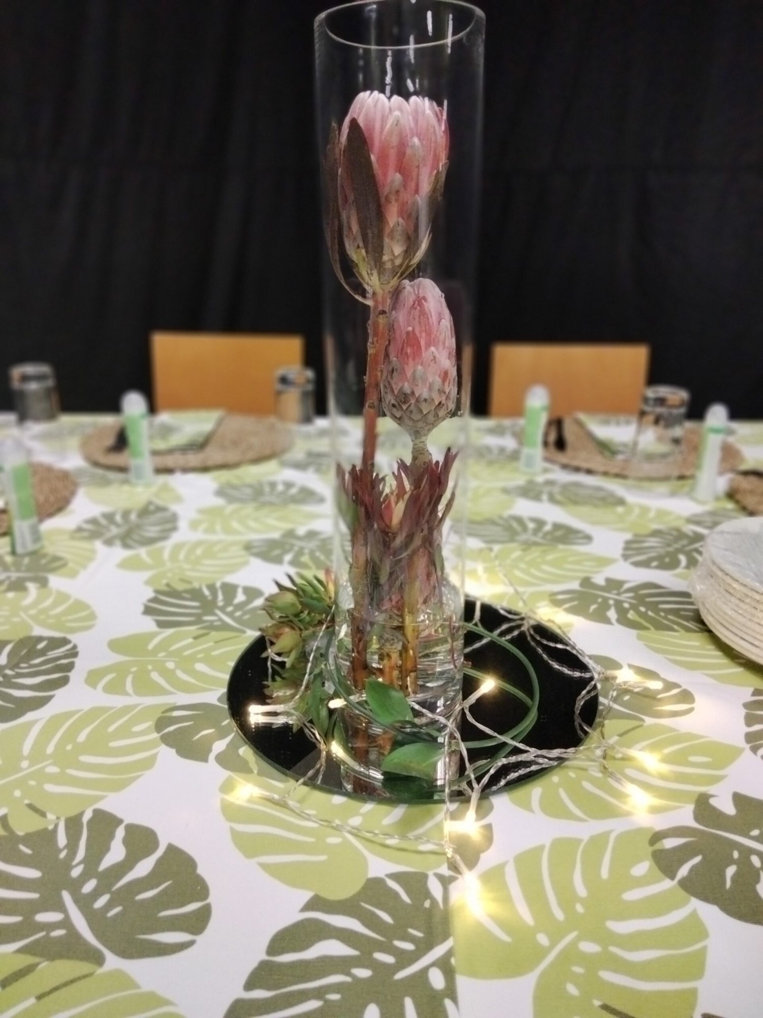 Table centerpiece featuring a protea in a glass vase with lights.