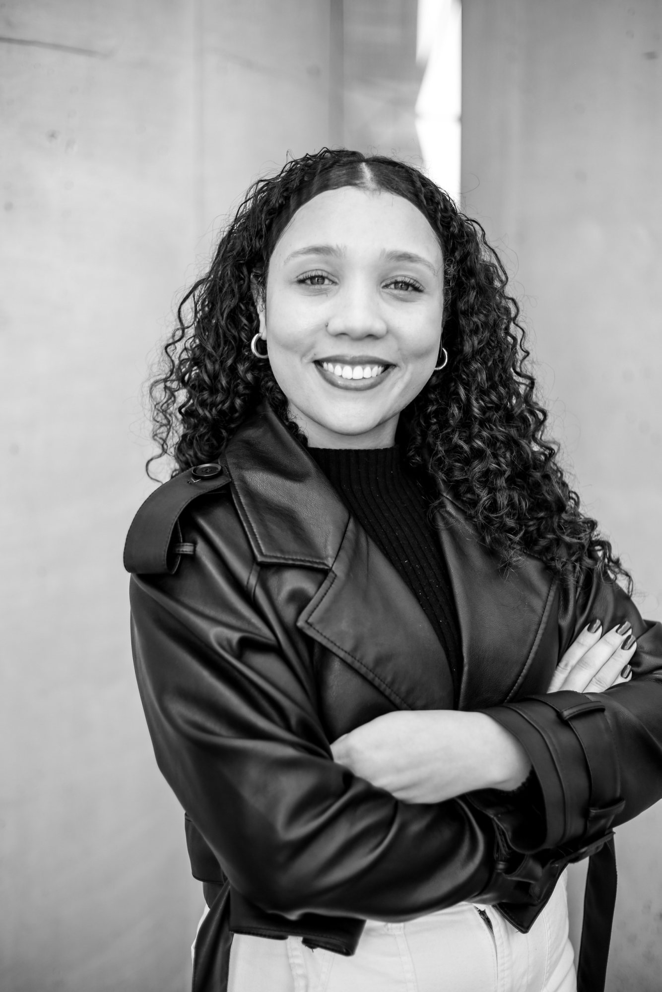 Black and white portrait of a smiling curly-haired woman in a leather jacket