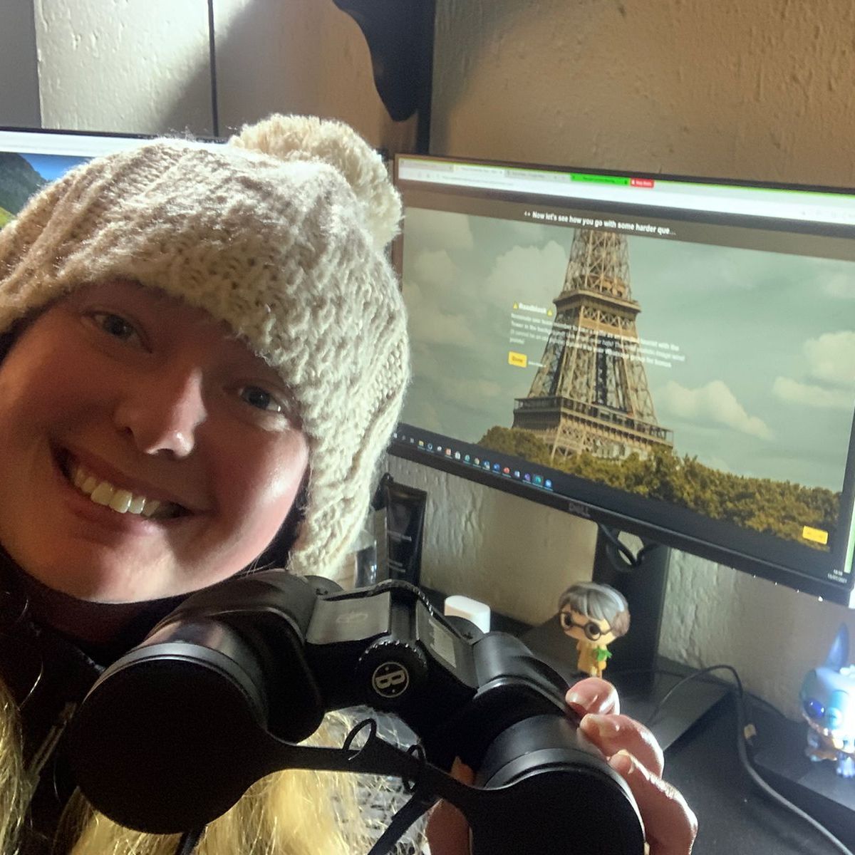 Person holding binoculars with an Eiffel Tower image on a computer screen