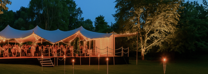 Outdoor stretch tent lit up at night with seating