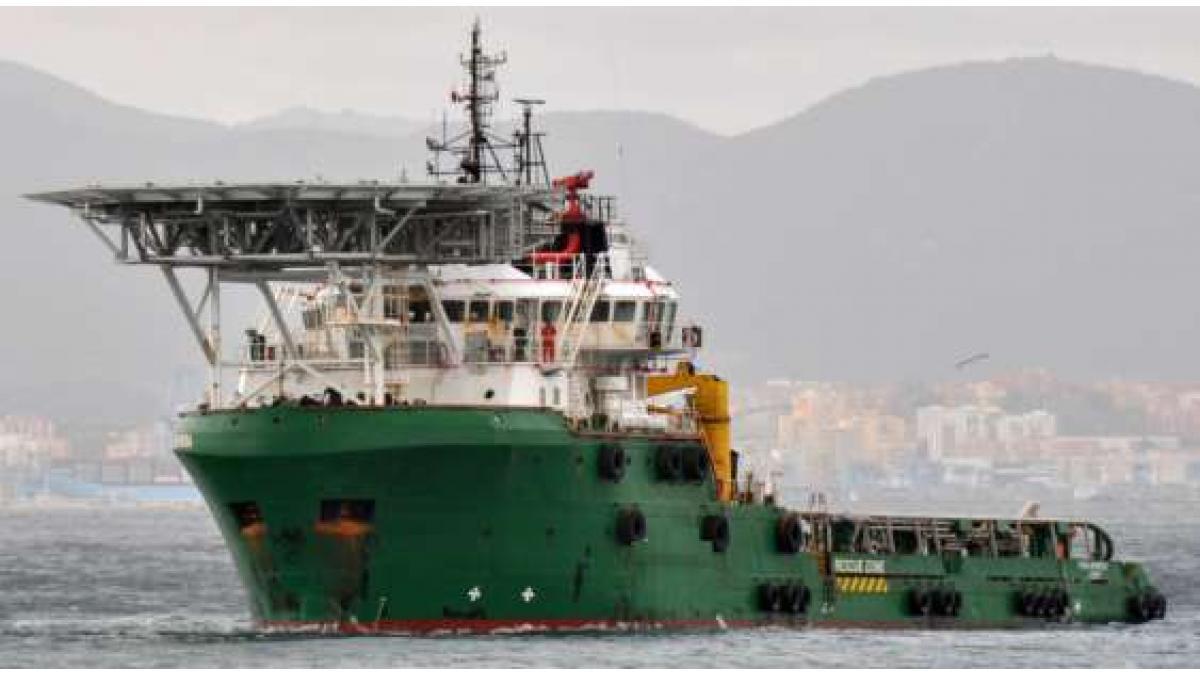 A large green ship at sea near a coastal city.