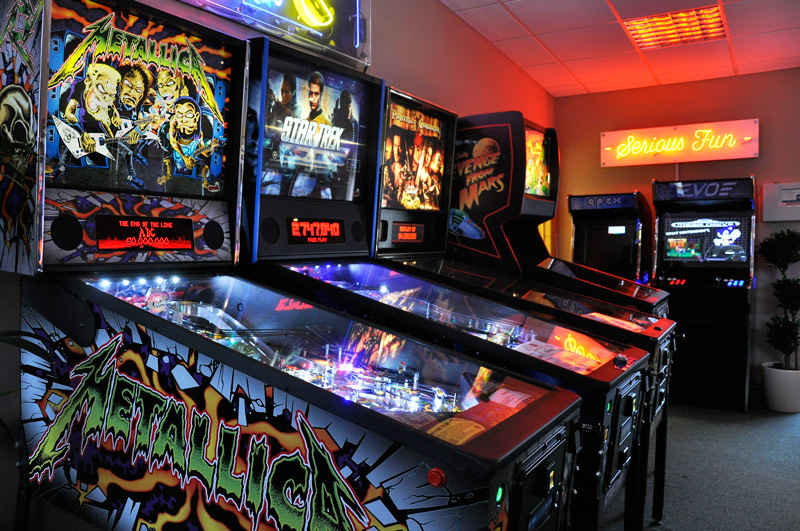 Row of brightly lit pinball machines in an arcade