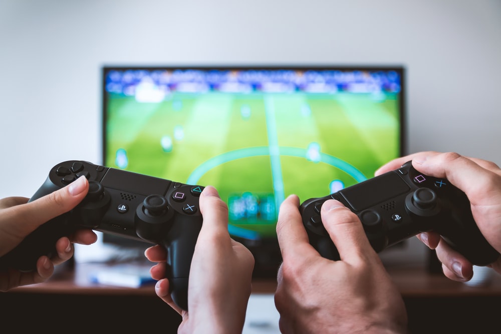 Two hands holding PlayStation controllers while gaming.