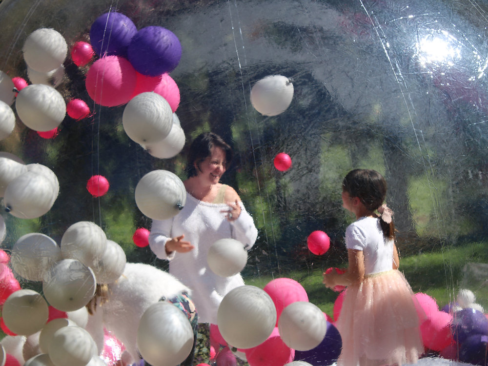 Two children interacting inside a colorful bubble house filled with balloons.
