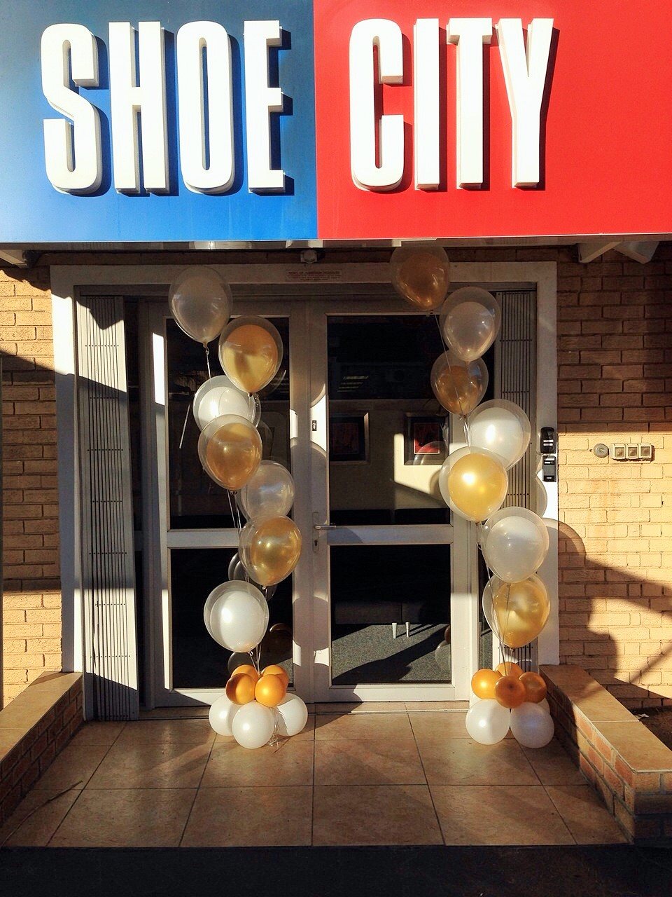 Balloon arch in gold, white, and clear at Shoe City entrance.