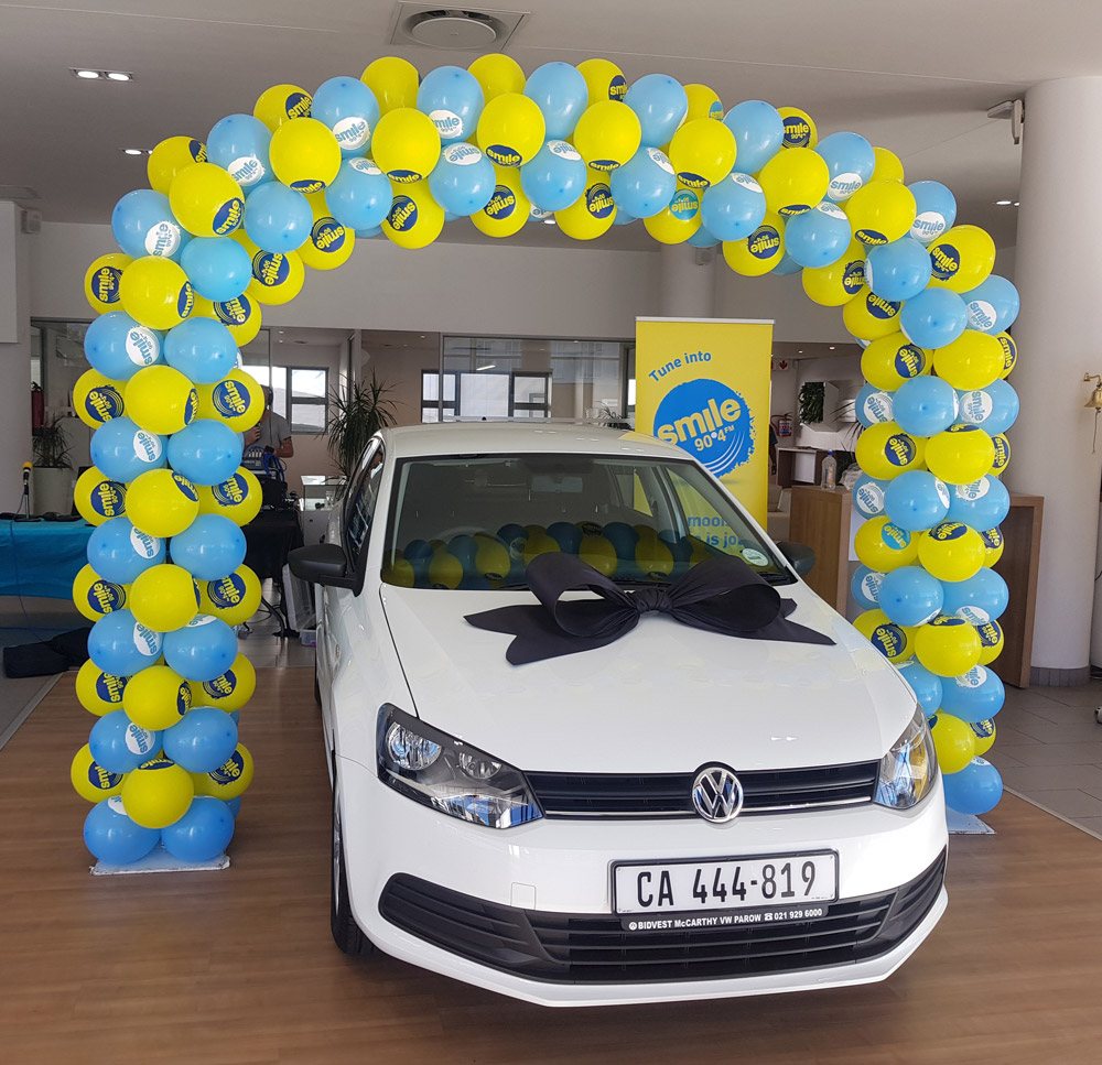 Colorful balloon arch in blue and yellow at a car dealership.