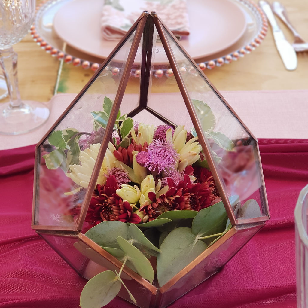 Glass terrarium with colorful flowers on a maroon tablecloth