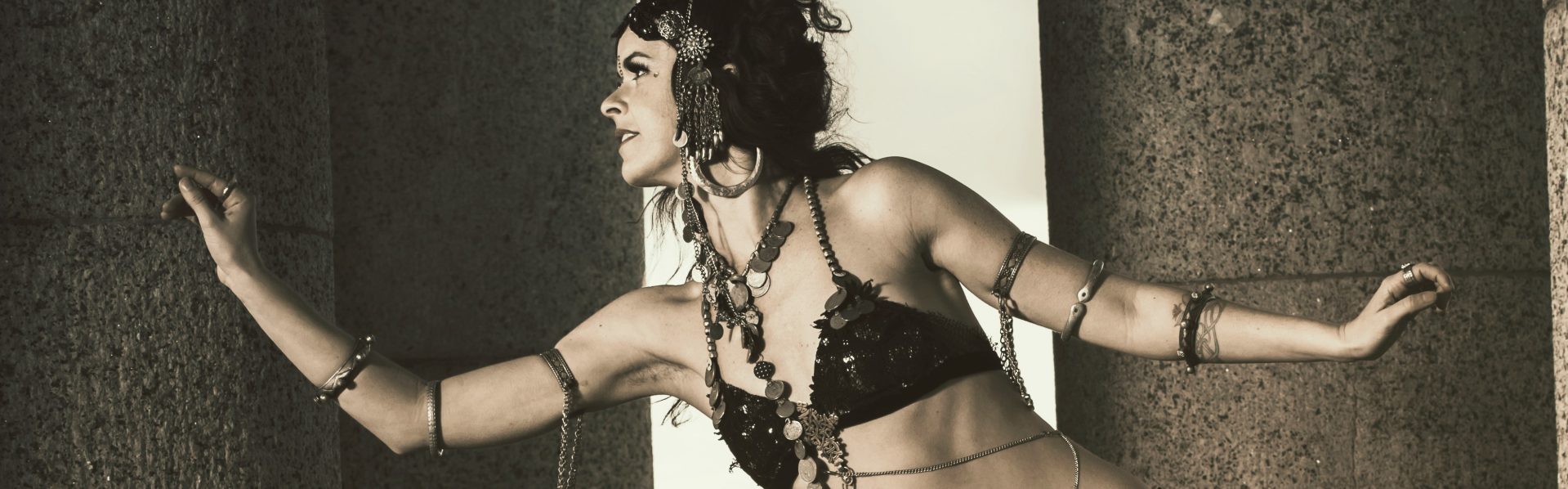 Belly dancer in intricate costume poses between stone columns.