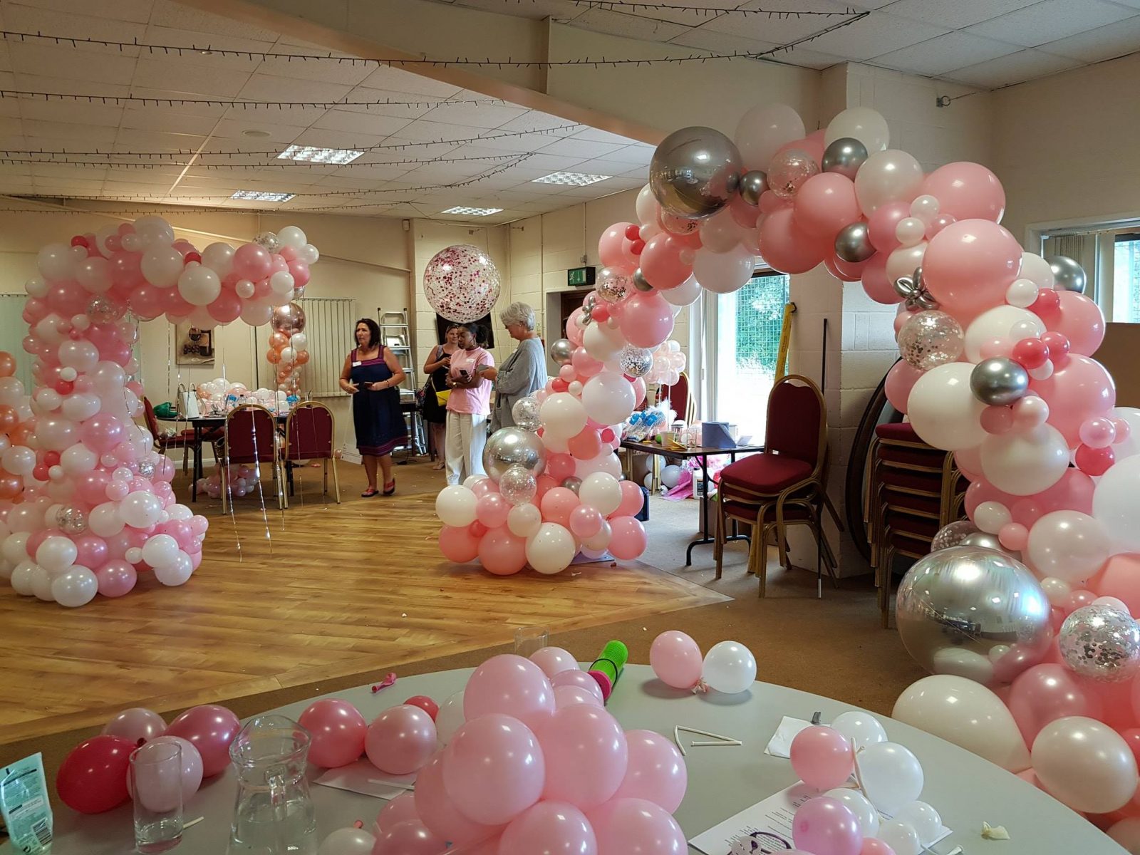 Two pink and white balloon arches in a decorated venue.