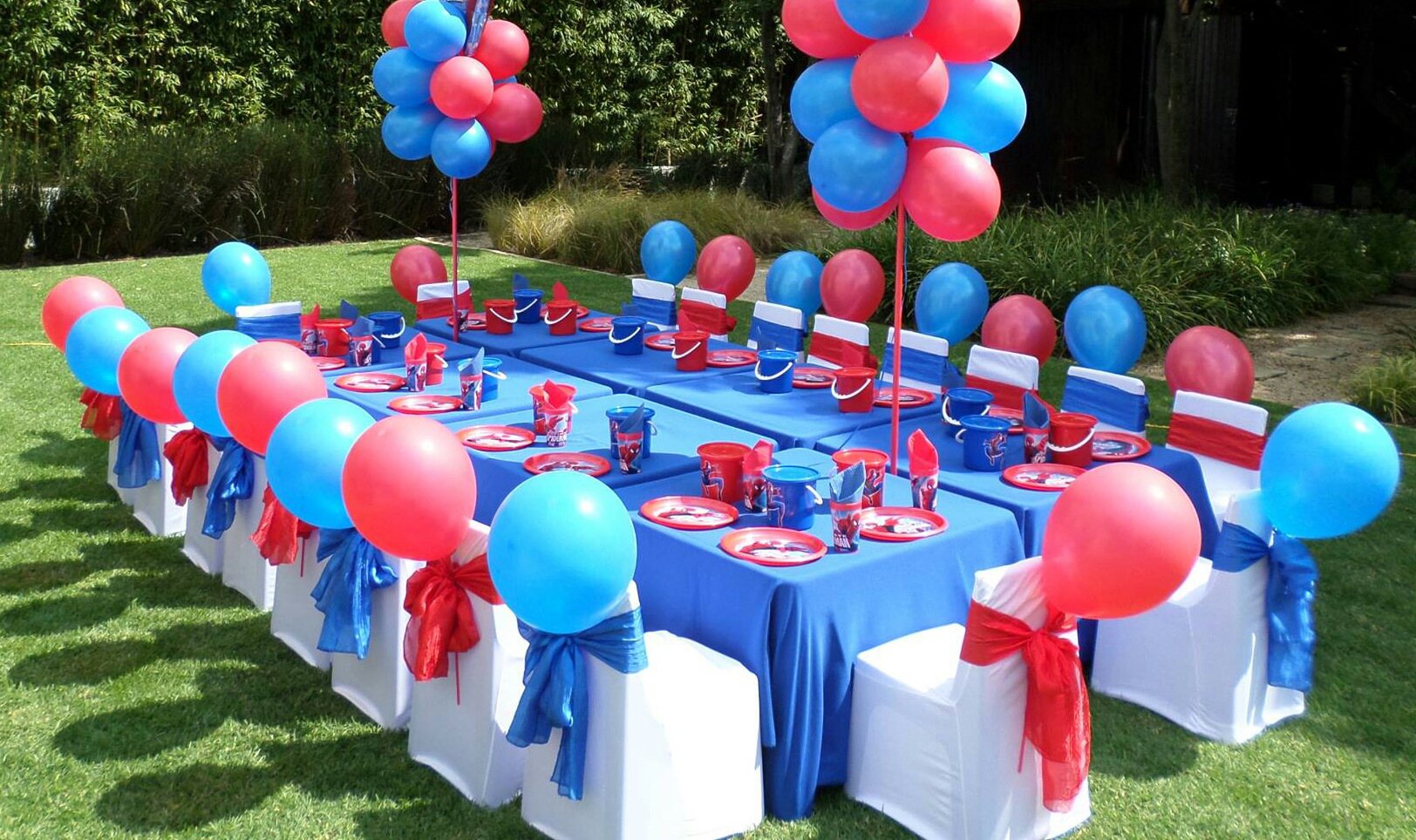 Outdoor party table with blue and red balloons and themed decor.
