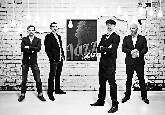 Four musicians dressed in formal attire with a jazz-themed backdrop