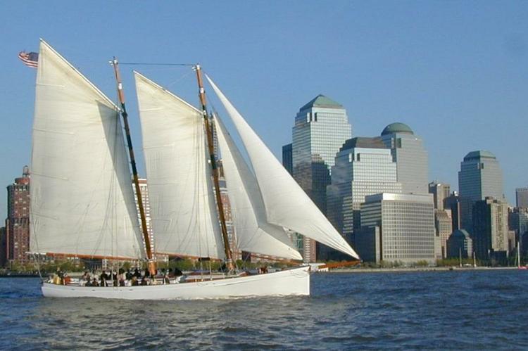 Sailboat with white sails near city skyline