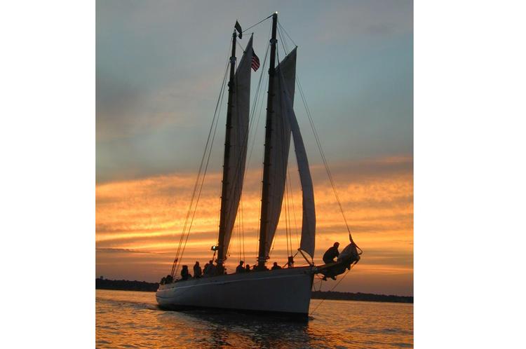 Sailboat with two sails on water during sunset