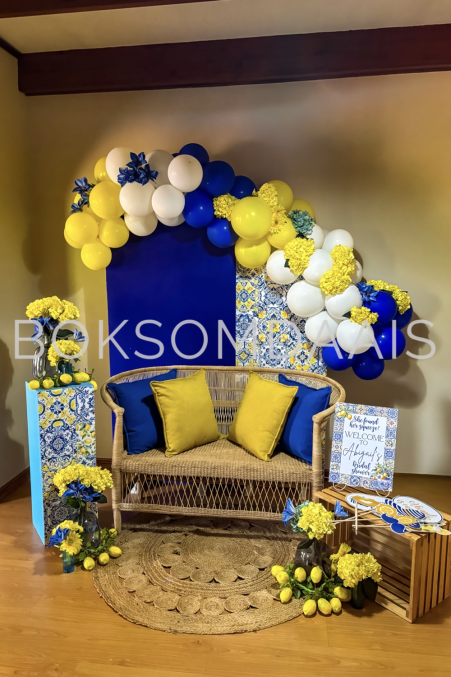 Event decor with rattan sofa, yellow cushions, and balloon arch.