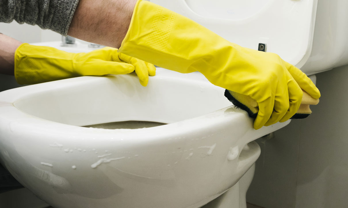 Person cleaning a toilet bowl with yellow gloves