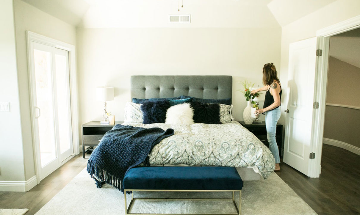 Modern bedroom with a bed, nightstand, and a person arranging decor.