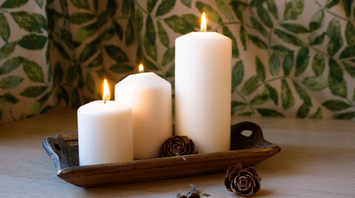 Three white pillar candles on a wooden tray with decorative elements