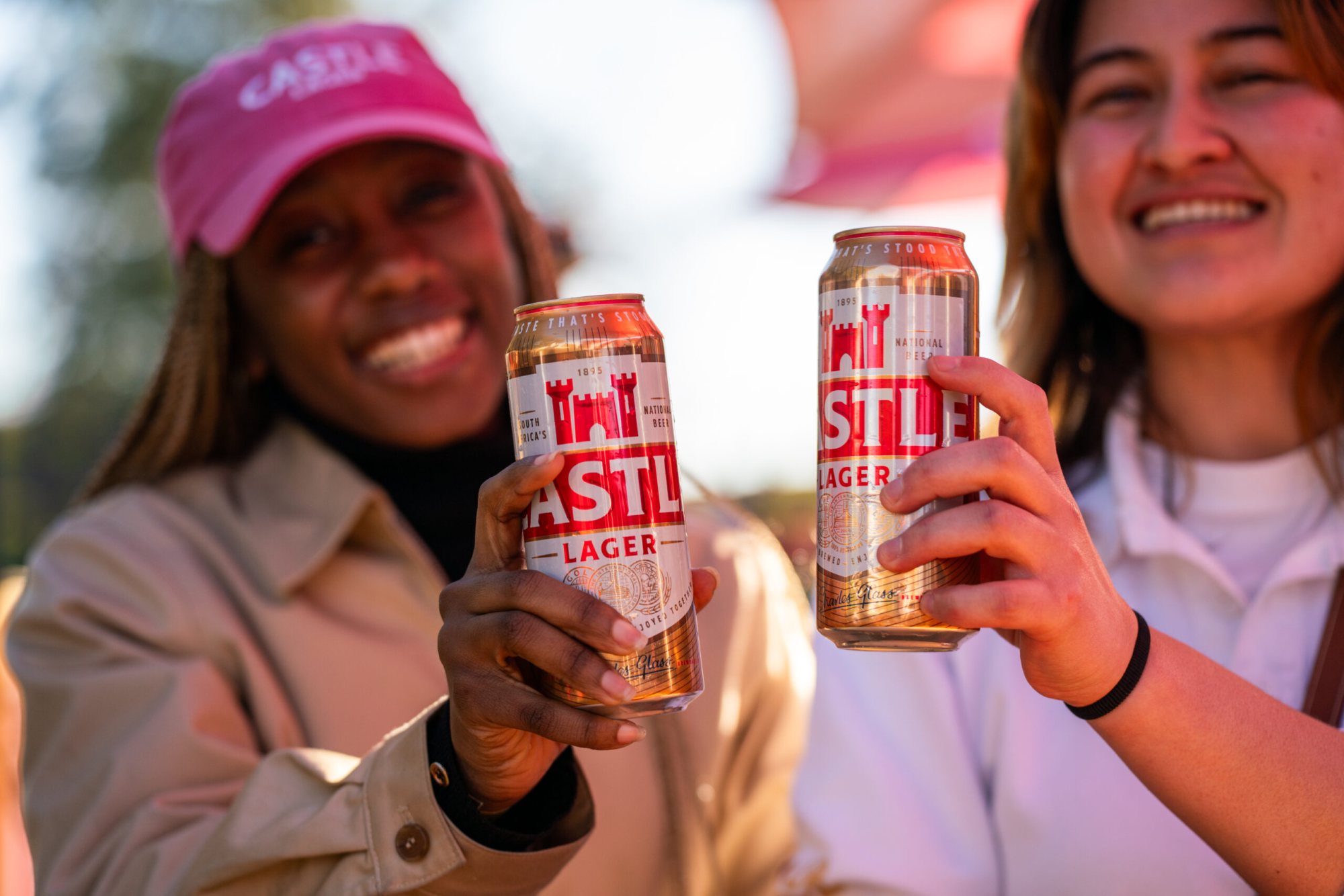 Two women holding Castle Lager cans and smiling.