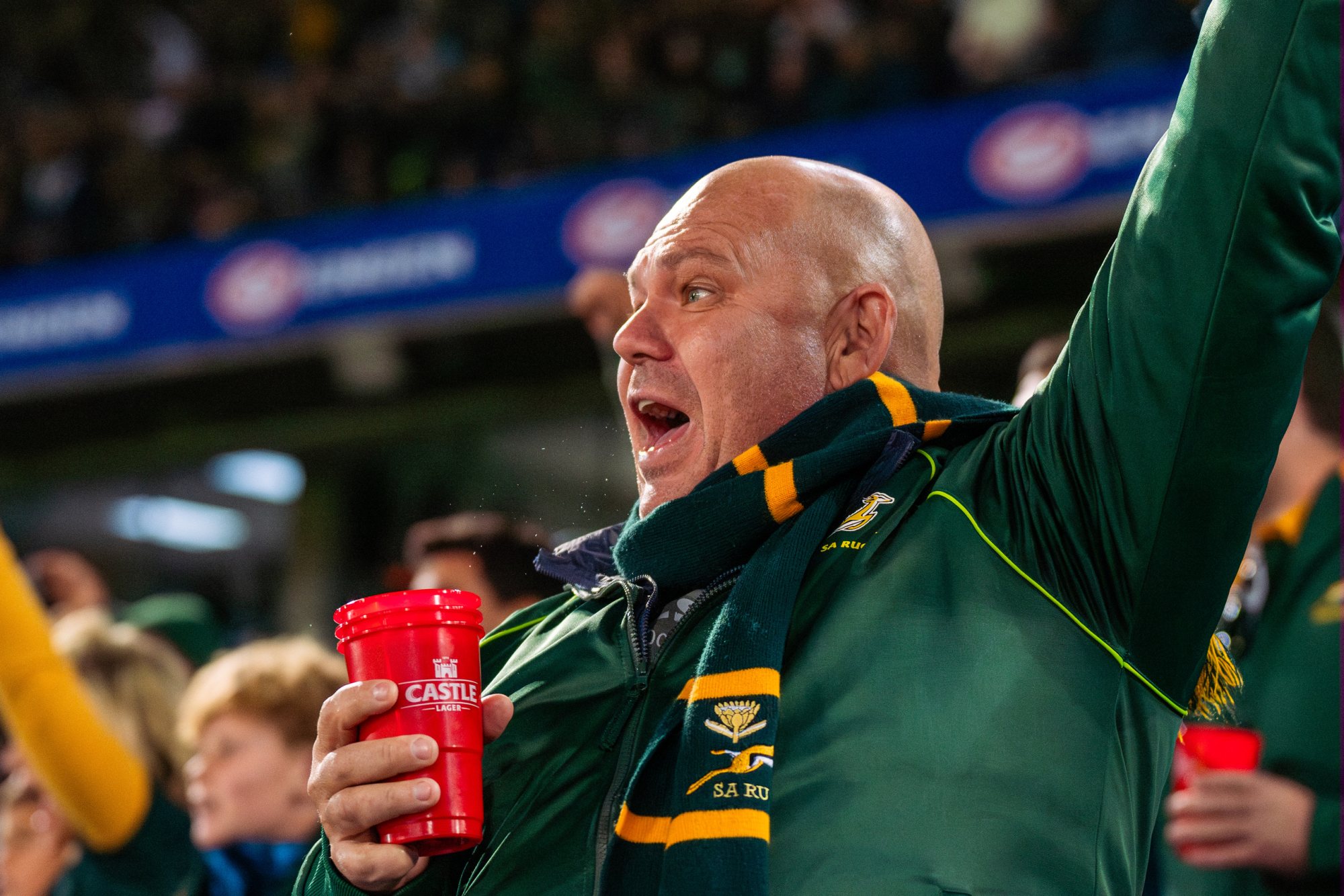 A passionate sports fan cheering with a drink in hand.