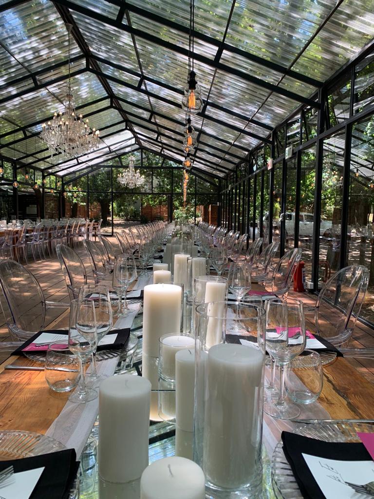 Long table set with white pillar candles and glassware in a greenhouse venue