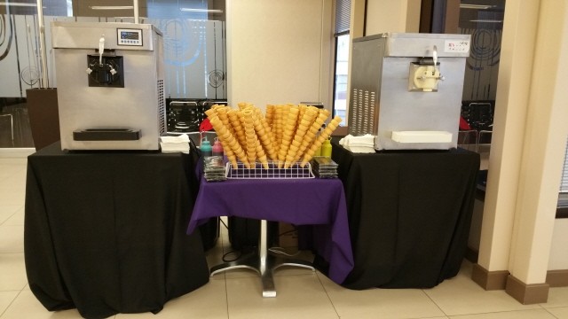 Two soft serve machines with ice cream cones and toppings