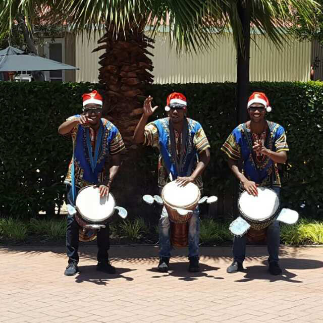 Three male drummers in traditional attire and Santa hats