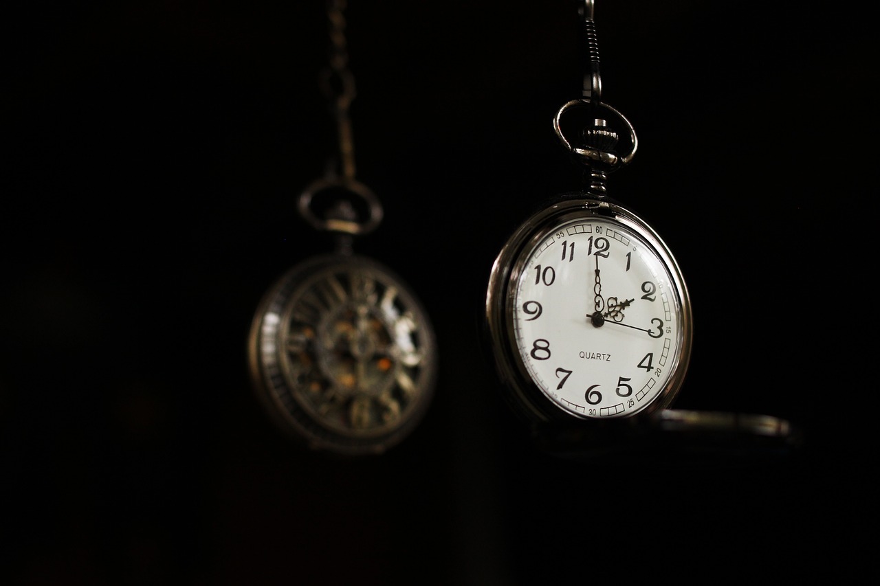 Two vintage pocket watches hanging against a dark background.