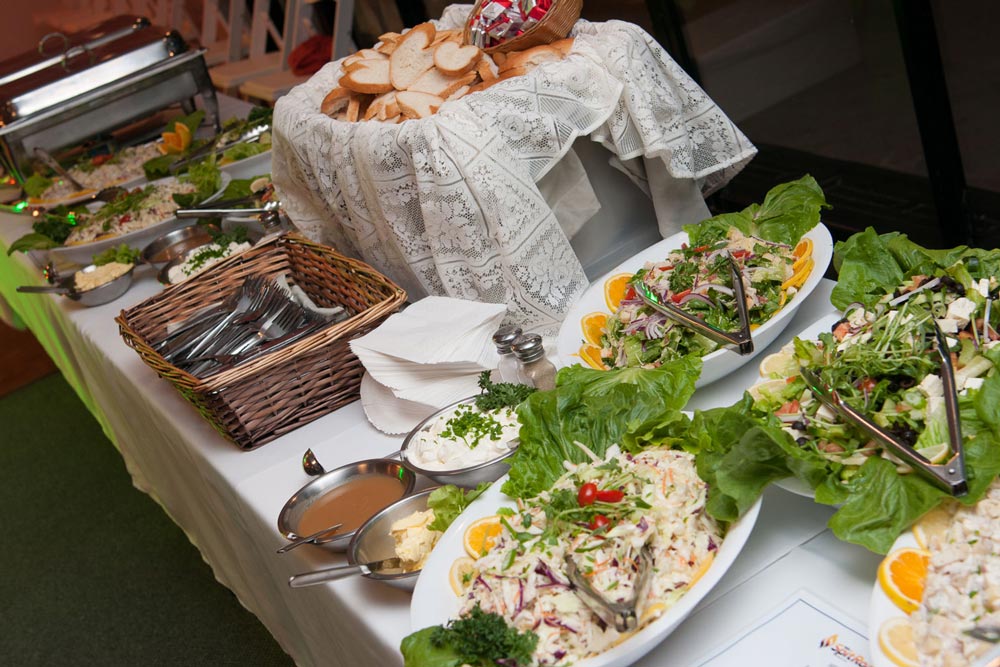 Buffet table featuring salads, bread, and utensils.