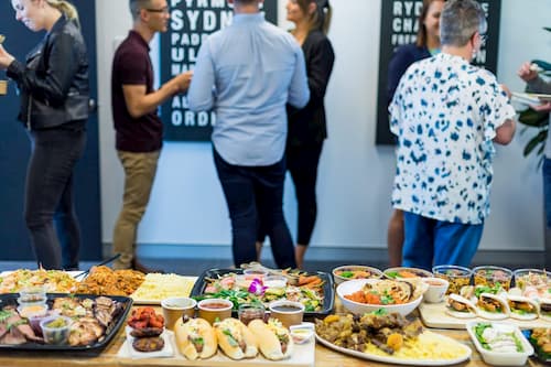 Buffet table with diverse food items and guests in the background