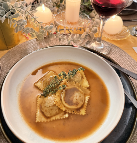 Bowl of ravioli in broth with herbs and wine glass