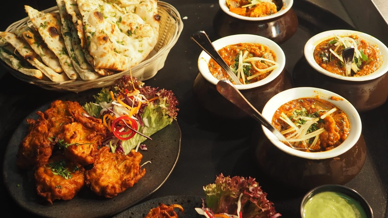 A spread of halaal dishes including naan, curries, and fritters