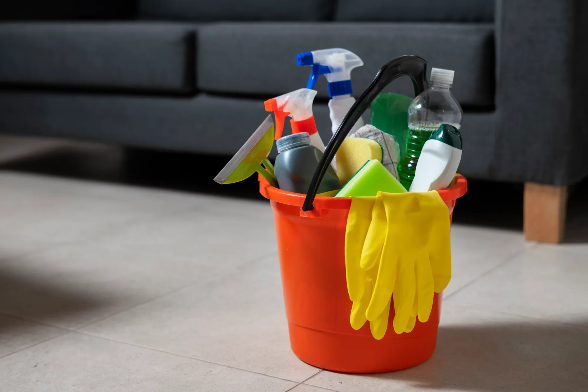 Orange bucket with cleaning supplies, gloves, and sponges.