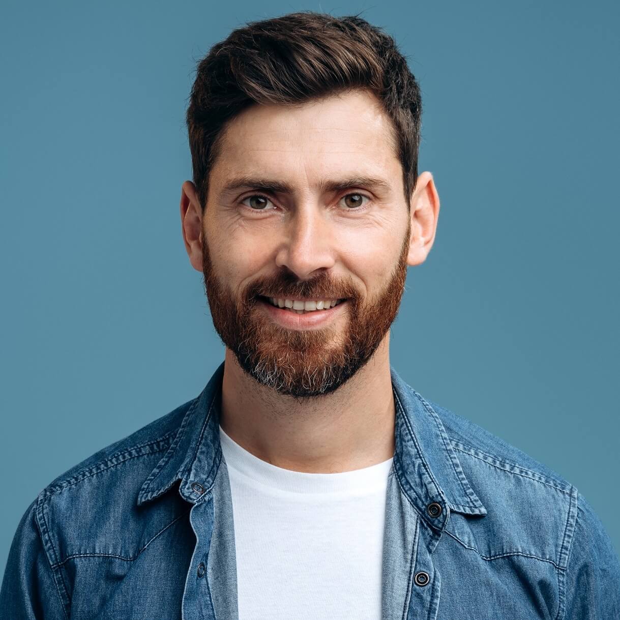 Smiling man in denim shirt against a blue background