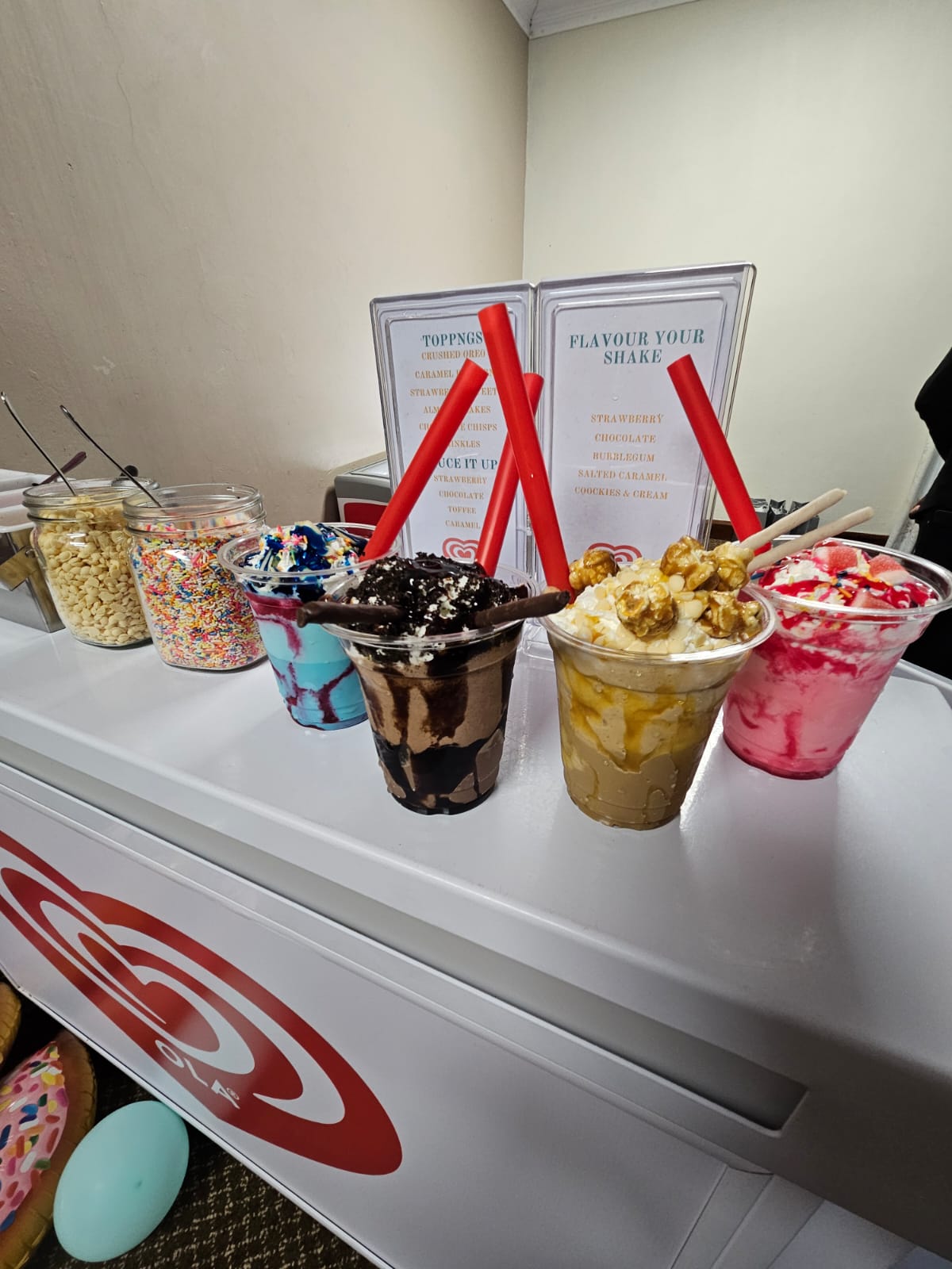 Colorful milkshakes in cups with toppings on a dessert bar.