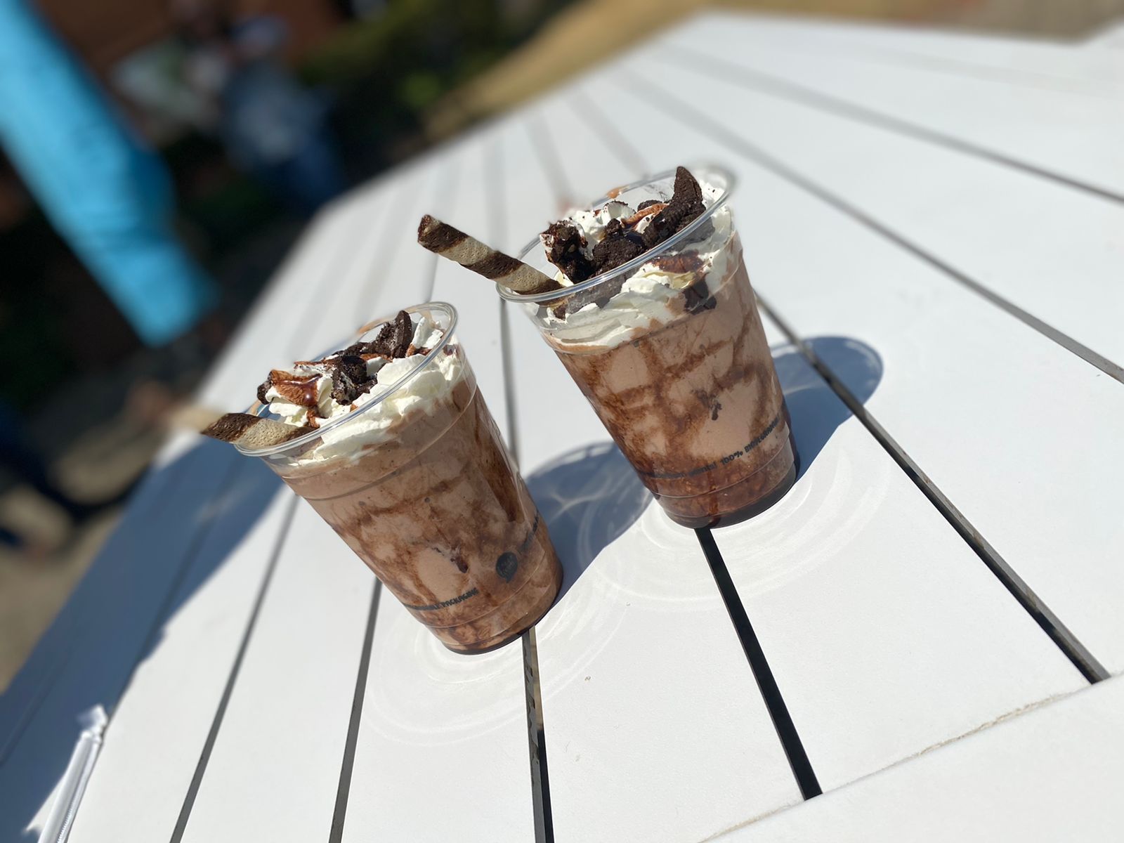 Two chocolate dessert shakes with whipped cream on a white table.