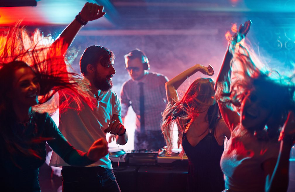 People dancing energetically at a party with a DJ.