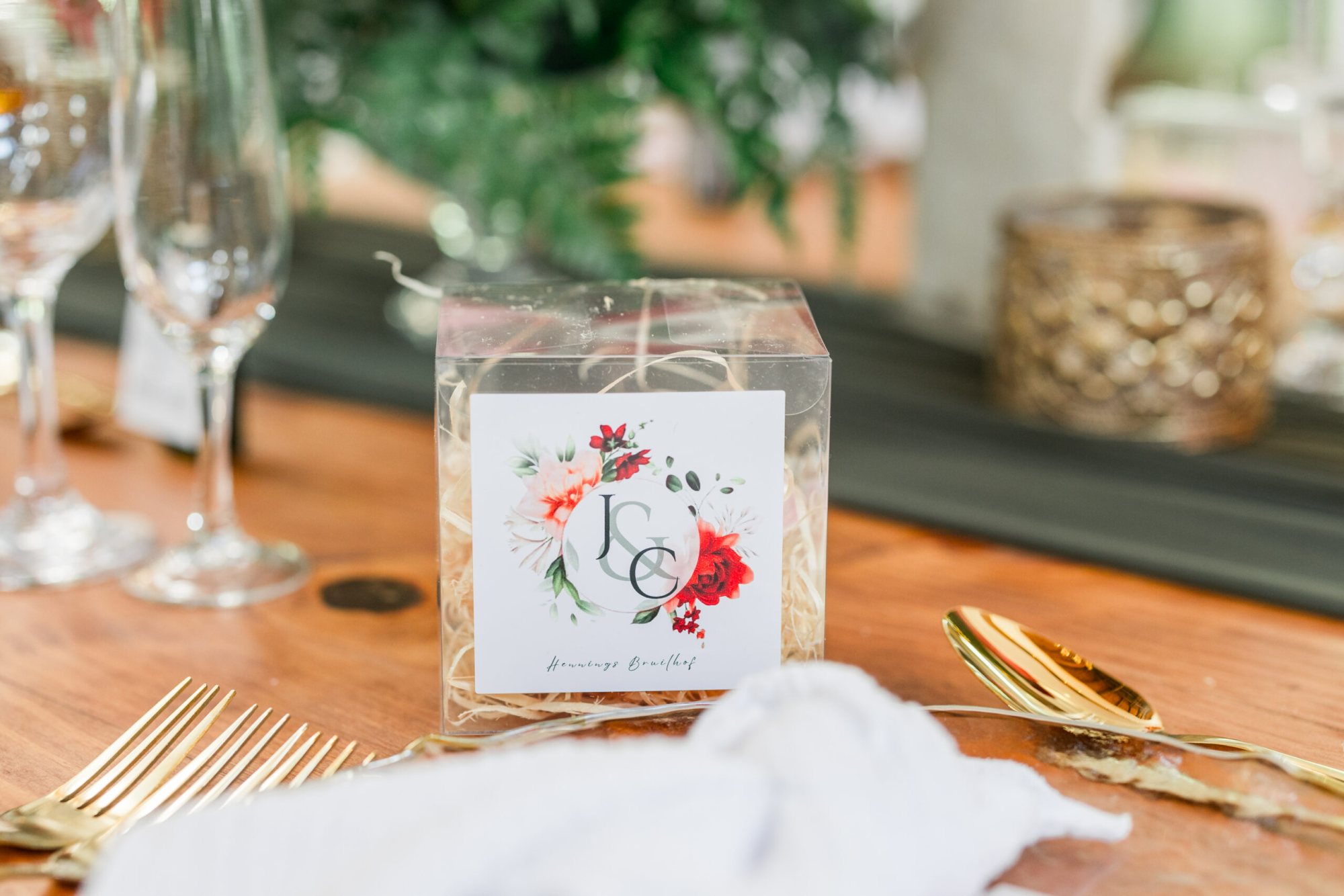 A clear favor box with a floral design and initials.