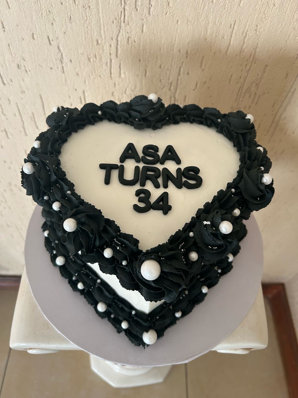 Heart-shaped birthday cake with black icing and white text.