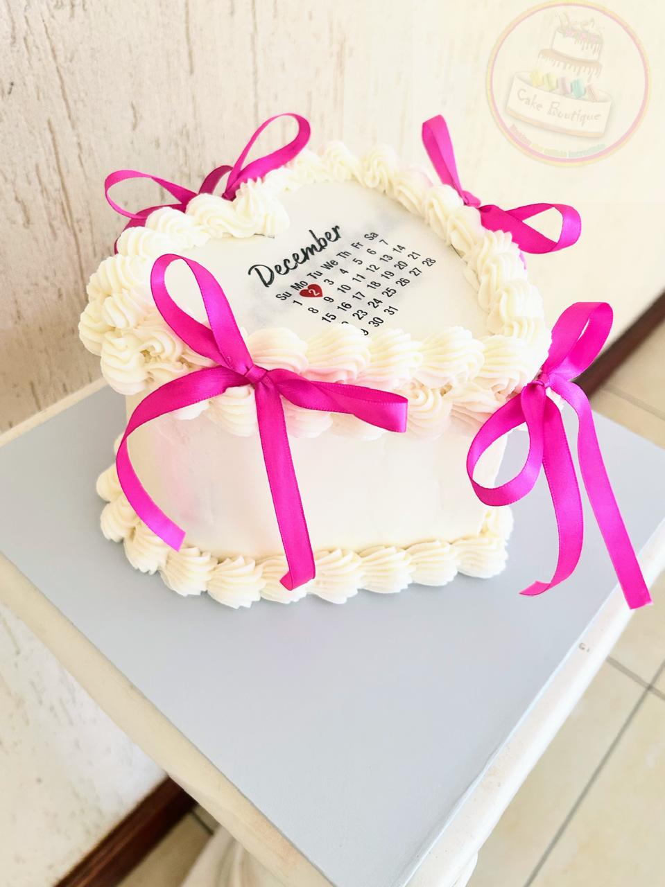 Decorative birthday cake with pink ribbons and a calendar design.
