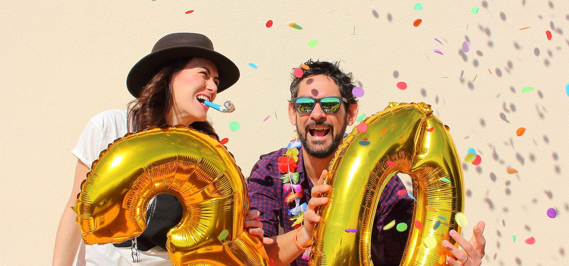 Two people joyfully holding gold balloon numbers 2 and 0, celebrating.