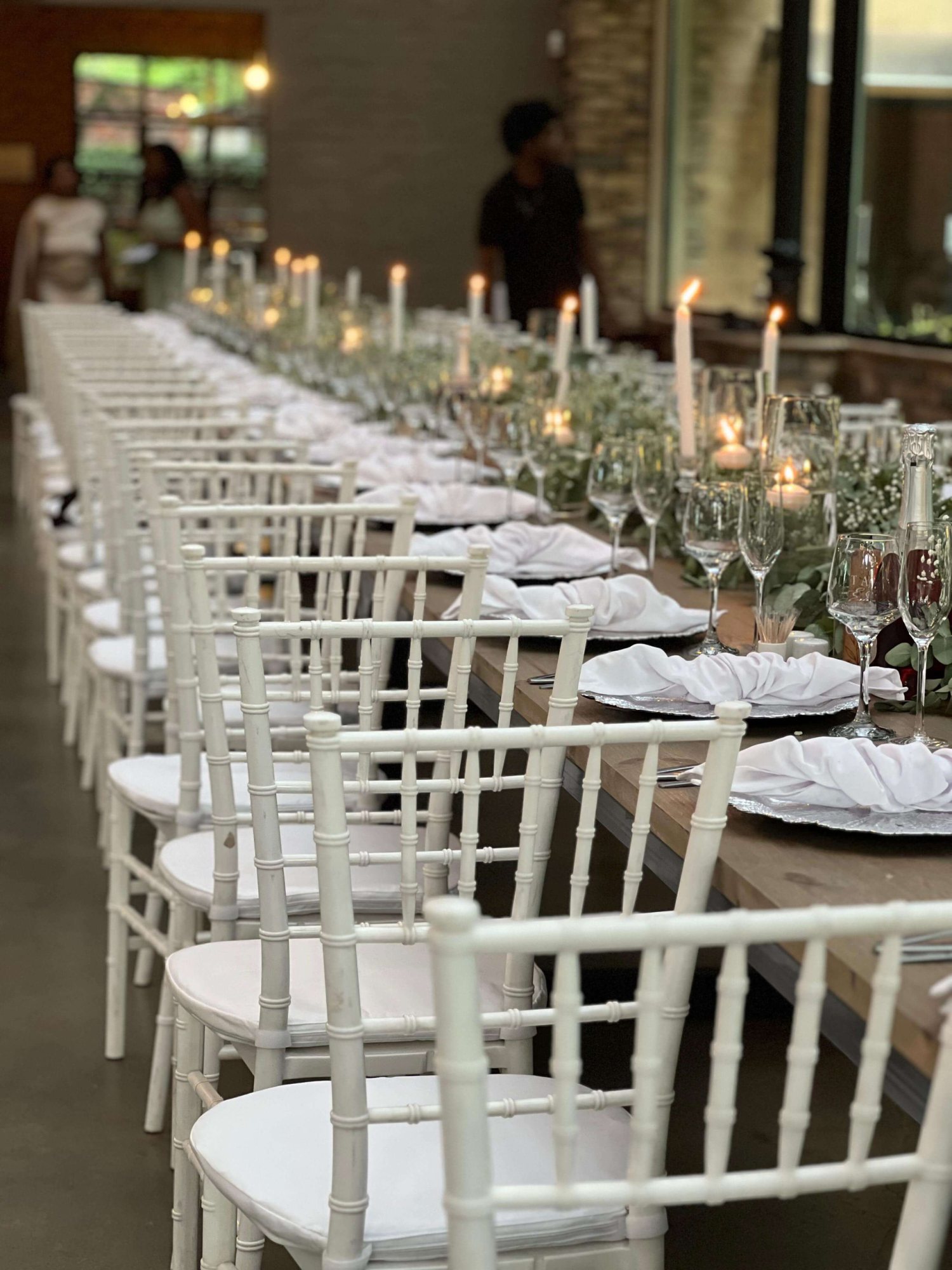 Long table set with white chairs, candles, and greenery