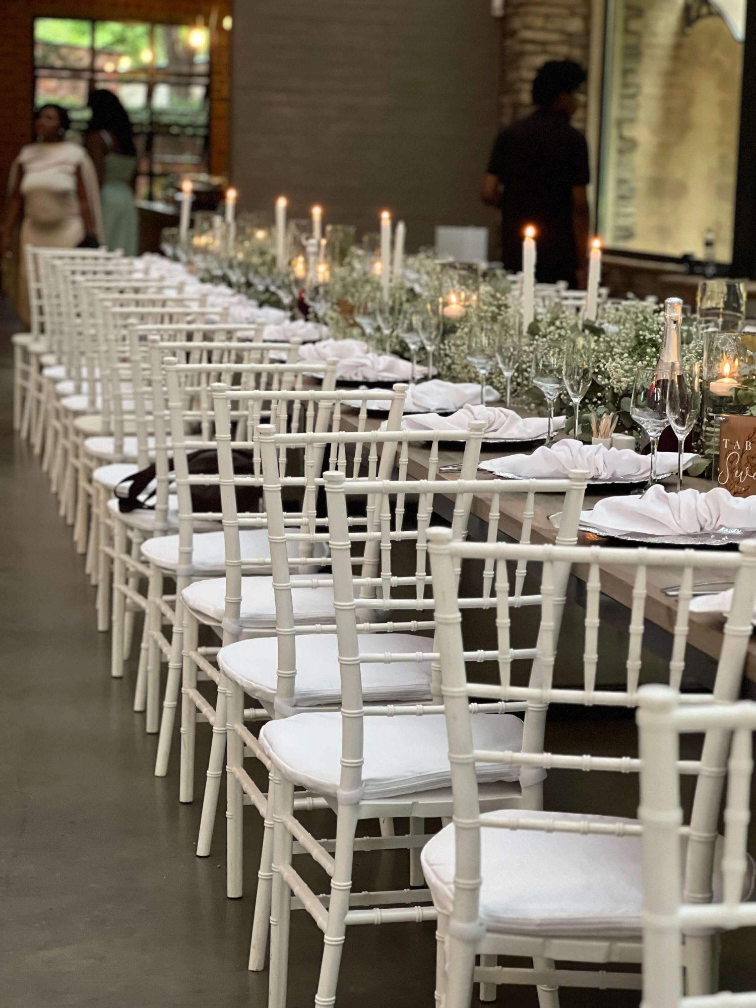 Long dining table set with white chairs and candles