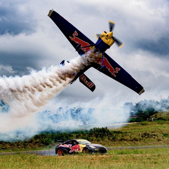 Drone shot of an aerobatic plane performing a stunt over a car.