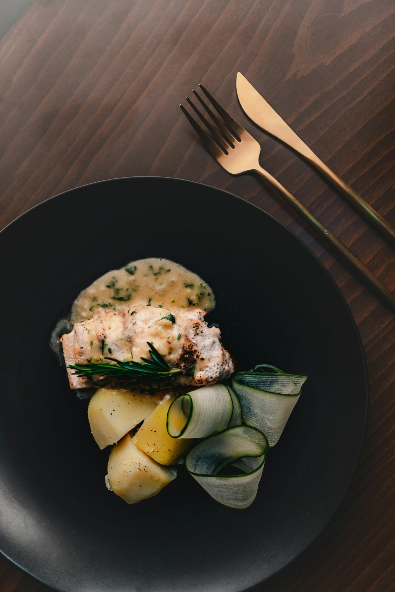 Plated fish dish with vegetables and sauce on a dark plate