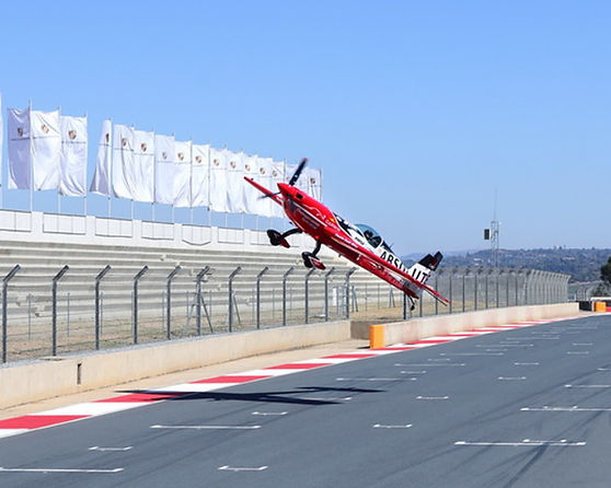 A red aircraft performing an aerial stunt over a race track.
