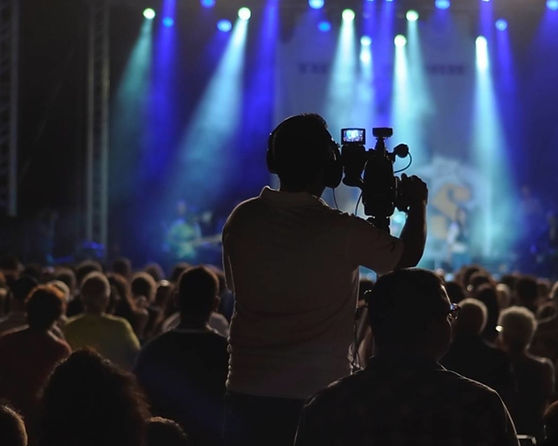 A videographer recording a live event with a crowd in the background.