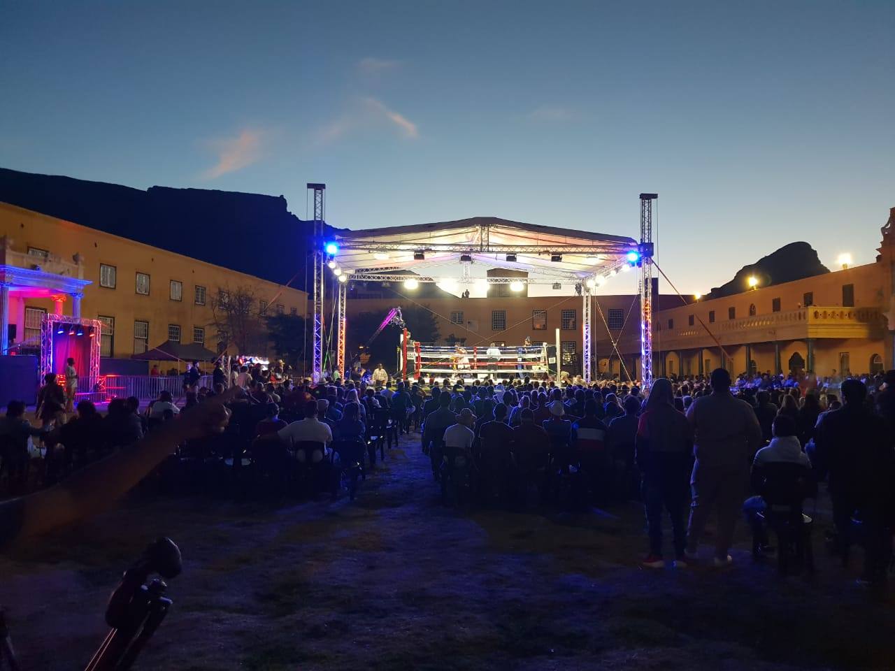 Outdoor event setup with audience gathered around a boxing ring