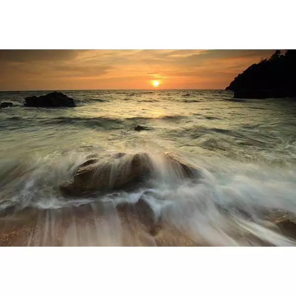 A stunning sunset over a beach with waves crashing on rocks.
