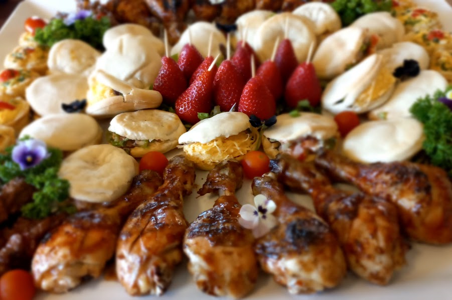 A colorful platter with chicken, desserts, and snacks arranged artistically.