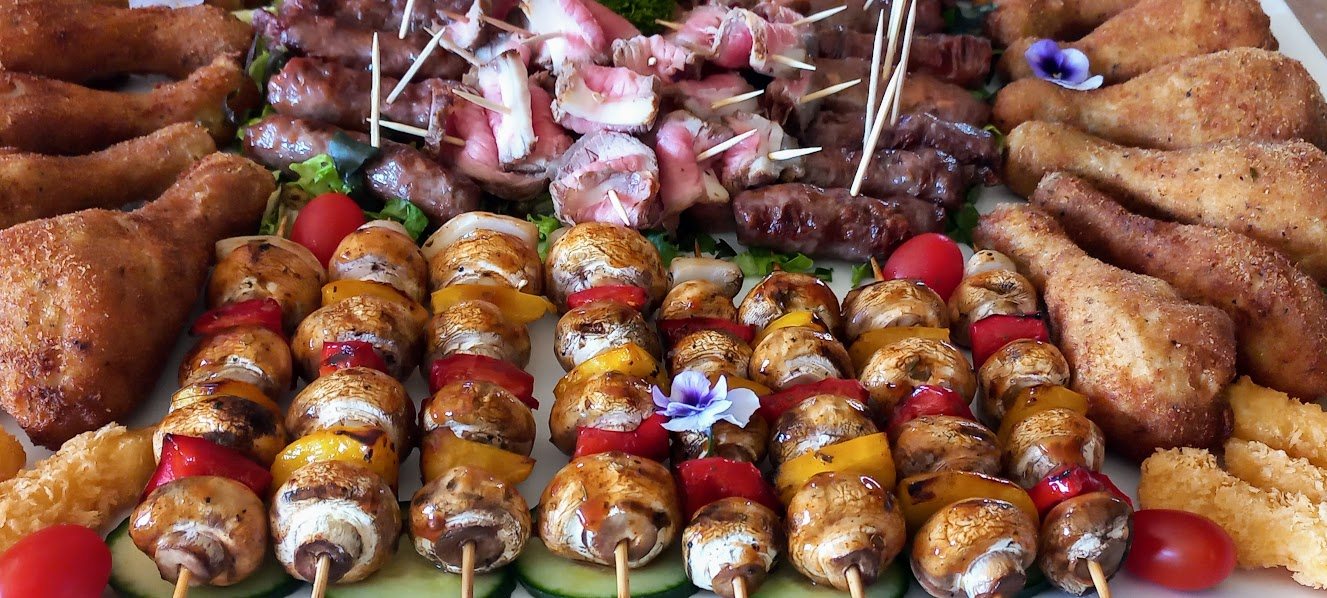 An assortment of finger foods including chicken drumsticks, kebabs, and mushrooms on skewers.